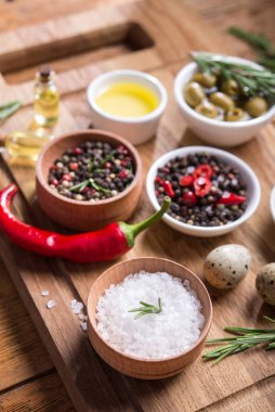 Taze salata malzemeleri (tuz, biber, zeytin, domates, biberiye, yağ) ahşap bir masa üzerinde kesim tahtasıyla birlikte.