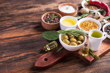 Taze salata malzemeleri (tuz, biber, zeytin, domates, biberiye, yağ) ahşap bir masa üzerinde kesim tahtasıyla birlikte.