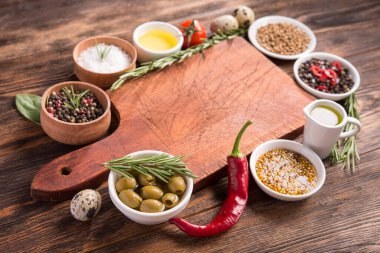 Taze salata malzemeleri (tuz, biber, zeytin, domates, biberiye, yağ) ahşap bir masa üzerinde kesim tahtasıyla birlikte.