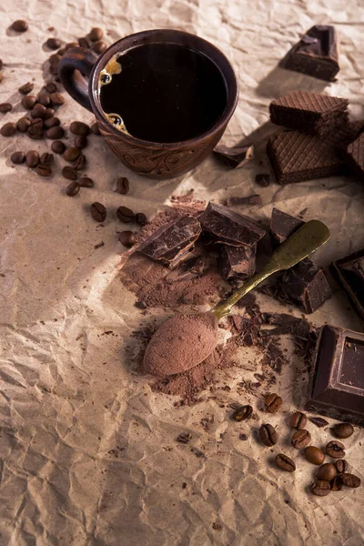 Büyük parça koyu çikolata, kakao tozu ve kağıt üzerinde kahve fincanı..