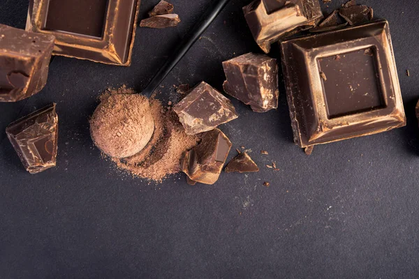 Büyük siyah çikolata parçaları ve siyah kaşıkta kakao tozu..