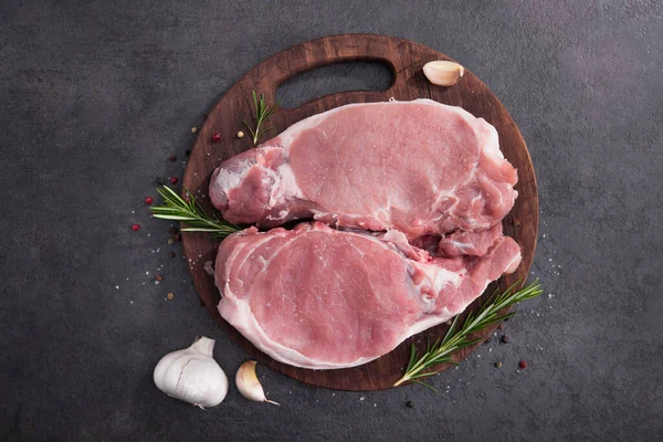 Ahşap bir tahtada çiğ domuz bifteği, baharatlar ve pişirmek için malzemeler. en üstteki görünüm.
