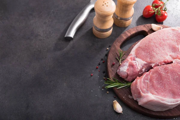 Ahşap bir tahtada çiğ domuz bifteği, baharatlar ve pişirmek için malzemeler. Metin için yer.