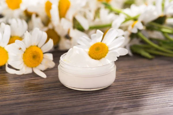 Masasında papatya kremi ve çiçek olan bir kap. kozmetik cilt ve vücut bakımı kavramı.