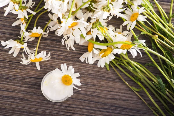 Masasında papatya kremi ve çiçek olan bir kap. Kozmetik deri ve vücut bakımı konsepti. en üstteki görünüm