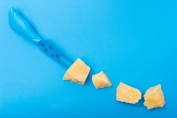 Tasty parmesan yellow cheese pieces on a blue background. Color and minimal concept.