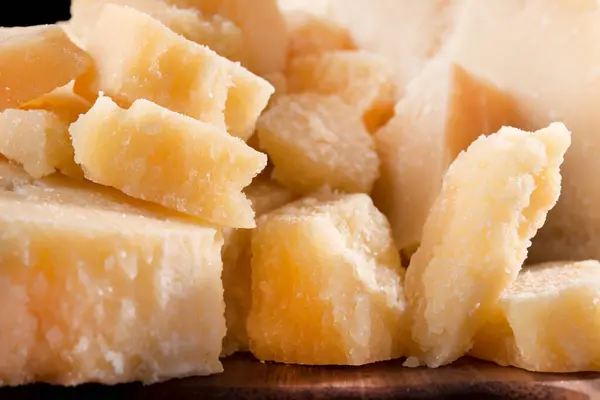 Parmesan peynirinin lezzetli ve taze parçalarını bölme tahtasında, siyah arka planda..