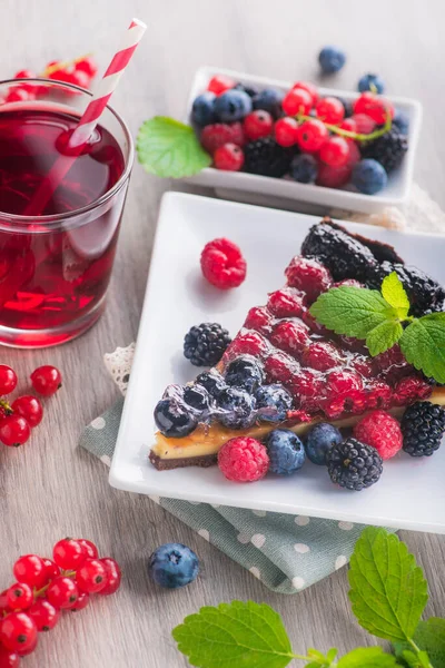 Taze böğürtlenli, ahududulu, üzümlü, yaban mersinli, yeşil naneli, ahşap masada kırmızı limonata içen tatlı pasta..