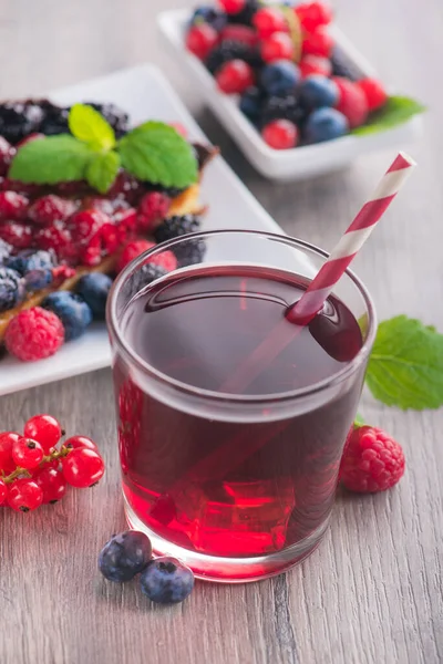 Taze böğürtlenli, ahududulu, üzümlü, yaban mersinli, yeşil naneli, ahşap masada kırmızı limonata içen tatlı pasta..