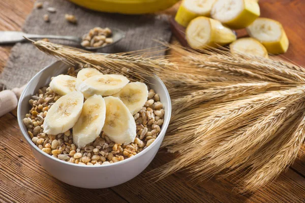 Tohum ve buğdaylı kasede gevrek gevrek, ahşap bir masada muz. Kırsal sağlıklı mısır gevreği Sabah kahvaltısı.