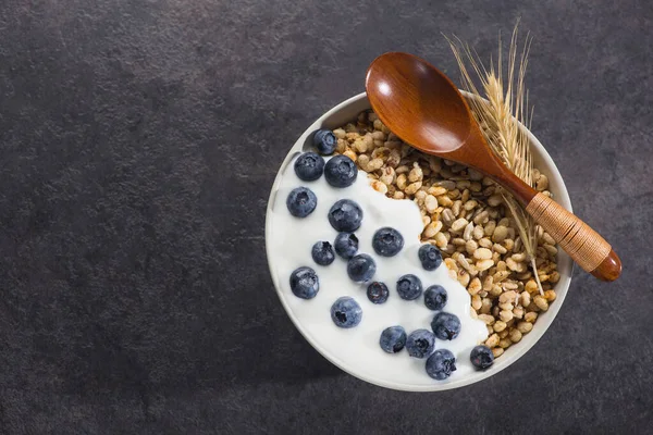 Bir kase ev yapımı gevrek yoğurt, taze yaban mersini ve arkaplanda buğday tohumu. Sağlıklı sabah kahvaltısı. en üstteki görünüm.