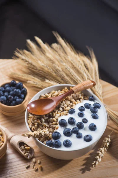 Bir kase ev yapımı tahıl gevreği yoğurt, taze yaban mersini ve ahşap bir masada buğday tohumu. Sağlıklı sabah kahvaltısı.