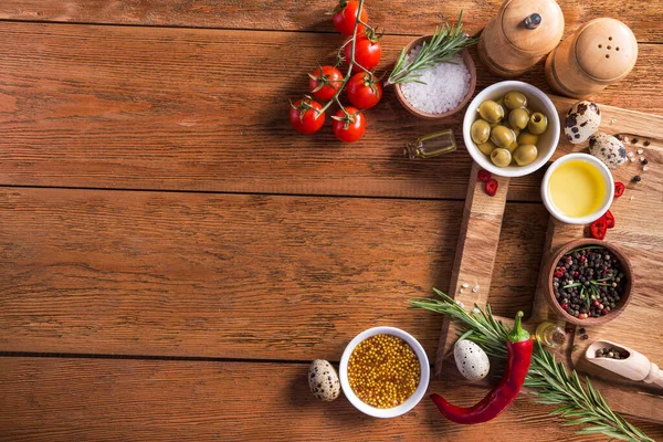 Taze salata malzemeleri (tuz, biber, zeytin, domates, biberiye, yağ) ahşap bir masa üzerinde kesme tahtasıyla birlikte. en üstteki görünüm