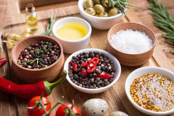 Taze salata malzemeleri (tuz, biber, zeytin, domates, biberiye, yağ) ahşap bir masa üzerinde kesim tahtasıyla birlikte.