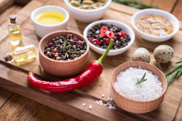 Taze salata malzemeleri (tuz, biber, zeytin, domates, biberiye, yağ) ahşap bir masa üzerinde kesim tahtasıyla birlikte.