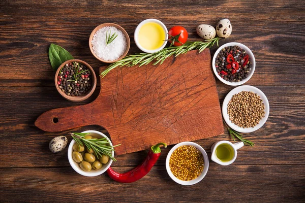 Taze salata malzemeleri (tuz, biber, zeytin, domates, biberiye, yağ) ahşap bir masa üzerinde kesme tahtasıyla birlikte. en üstteki görünüm