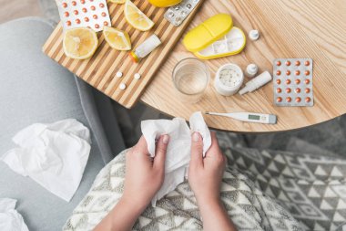 Soğuk algınlığı ve grip olan genç bir kadın. Evde kendi kendini tedavi ediyor. Vitamin ve haplarla. Alerji yüzünden burnu ağrıyor. en üstteki görünüm