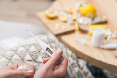 Soğuk algınlığı ve grip olan genç bir kadın. Evde kendi kendini tedavi ediyor. Vitamin ve haplarla. Alerji yüzünden burnu ağrıyor. Vücut ısısını ölçer