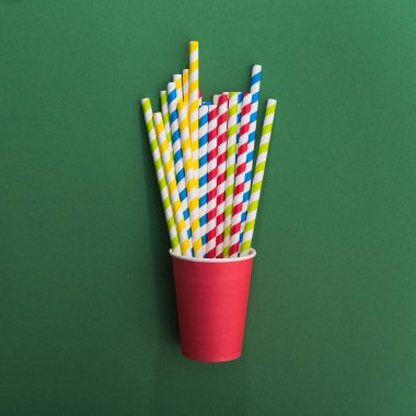 Yeşil arka planda kağıt bardakta parlak renkli kokteyl pipeti. Geri dönüşüm ekosu konsepti. Pop sanat tarzı. Düz yat. üstte