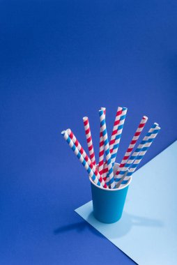 Mavi arka planda kağıt bardakta parlak renkli kokteyl pipeti. Geri dönüşüm ekosu konsepti. pop sanat tarzı.