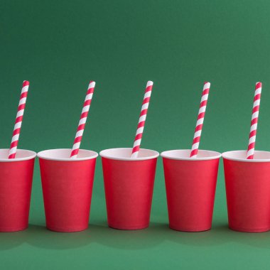 Yeşil arka planda, kağıt bardakta parlak kırmızı bir kokteyl pipeti. Geri dönüşüm ekosu konsepti. pop sanat tarzı.