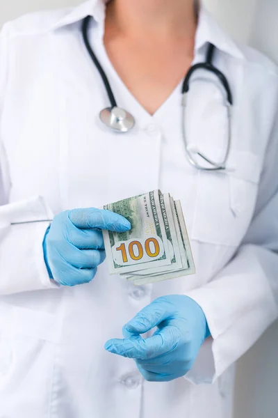 Doctor in clinic with a bundle of dollar bills. Corruption and bribery in medicine. Paid treatment.
