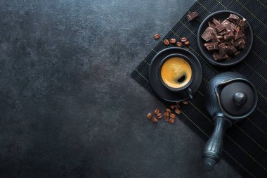 Siyah seramik bir fincanda Türk espresso kahvesi, taş bir masada çikolata. Uzayı kopyala Üst görünüm.