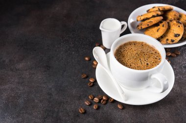 Çikolata parçalı kurabiyeli kahve fincanı, sütlü soslu, koyu taştan arka planda. Boşluğu kopyala