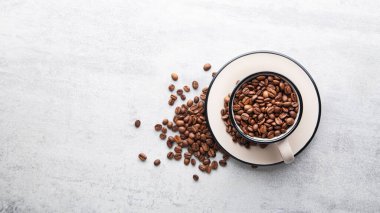 Taştan bir arka planda kavrulmuş kahve çekirdekleriyle dolu bir fincan. Sancak boyutu. Geniş biçim.