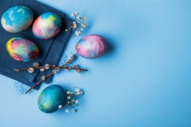 Mavi arka planda bahar çiçekleri olan mistik renkli yumurtalar. Paskalya tatili konsepti. en üstteki görünüm
