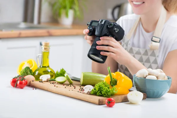 Woman food blogger shoots content on the camera in kitchen with fresh vegetables on a table. Blog about healthy eating. Step by step recipes dishes.