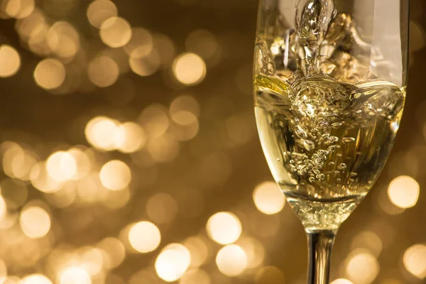 闪闪发光的白色香槟倒入一个玻璃杯中 放在一个金色的酒桶的背景上 圣诞及新年假期庆祝活动 — 图库照片