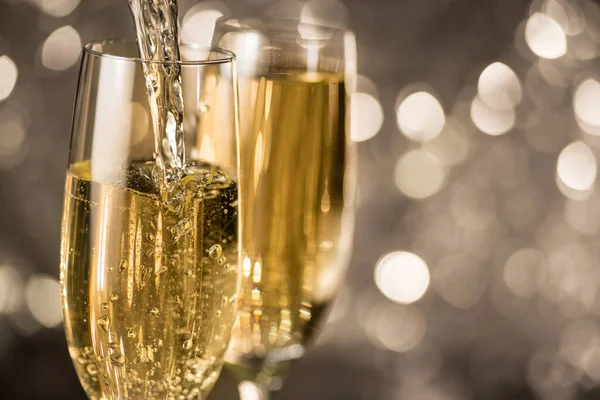 Köpüklü beyaz şampanya altın bir bokeh yuvarlak arka planda bir bardağa dökülür. Noel ve Yeni Yıl kutlamaları.