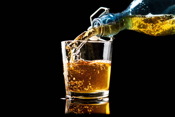 Pouring fresh gold apple cider in a glass on a black background