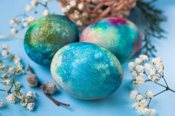 Mavi arka planda bahar çiçekleri olan mistik renkli yumurtalar. Paskalya tatili konsepti.