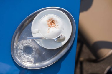 Mavi restoran masasında köpüklü kahve fincanı.