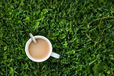 Soğuk bir sabahta, yeşil çimlerin üzerinde çiğ arkaplanlı sıcak bir fincan kahve.