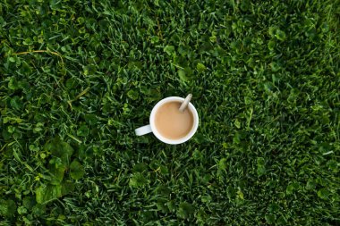 Soğuk bir sabahta sıcak bir fincan kahve, yeşil çimlerin üzerinde çiğ arkaplan, üst manzara