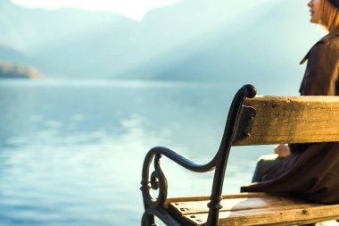 Kız Hallstatt Gölü 'nün yanındaki bankta oturuyor, gün batımında dağda.