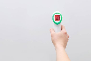 Elinde elektronik termometre tutan kadın doktor beyaz arka planda kameraya bakıyor. Hastalık konsepti ve koronavirüs salgınının belirtileri.