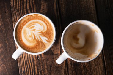 Bir fincan dolusu cappuccino ve ahşap zemin üzerinde boş bir fincan kahve. en üstteki görünüm
