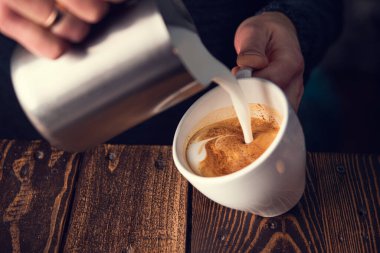 Barista taze süt koyar ve kafede kahve kapuçino yapar.