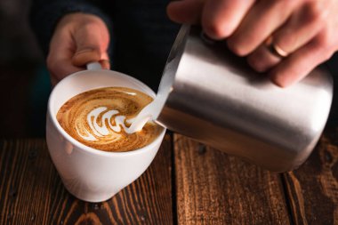 Barista kapuçino bardağına süt dolduruyor. Latte sanat arkaplanı.