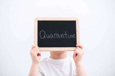 Çocuk, beyaz bir arka planda elinde bir karantina plakası tutuyor. Coronavirus konsepti. Örtülü yüz.