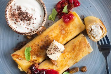Tereyağlı, reçelli ve ekşi kremalı krepler, arka planda nane yaprakları. en üstteki görünüm