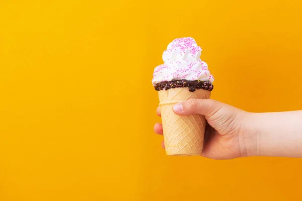 黄色の背景にワッフルアイスクリームを持つ子供の男の子の手 — ストック写真