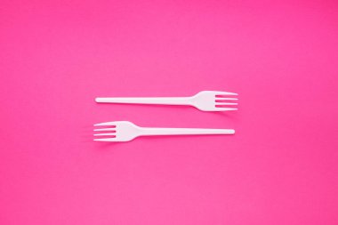 Popüler sanat tarzında pembe arka planda iki beyaz plastik çatal..