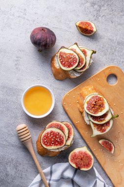 Krem peynirli çıtır çörek ve taze dilimlenmiş incir, susam tohumu ve taş zeminde bir kase bal. Üst Manzara. Düz Yat.