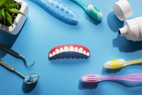 クリニックで青いテーブルの上の顎のプロテーゼ 歯磨き粉 歯ブラシ 歯科用ツールをモデル化します トップビューの背景 平置き — ストック写真