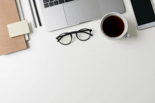 Vista superior del lugar de trabajo de la oficina. Escritorio blanco con espacio para copias. Vista plana en la mesa con ordenador portátil, teléfono, cuadernos, vasos, almohadillas de notas, taza de café y bolígrafos. Concepto de diseñador creativo . — Foto de Stock